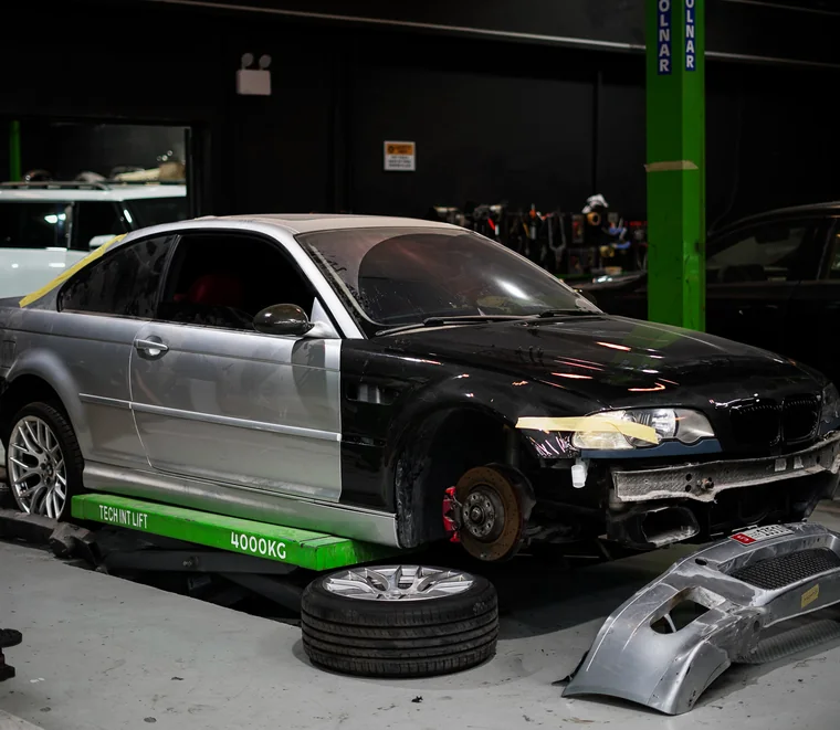 BMW coupe on a scissor lift with the wheels and front bumper removed for suspension and body work in Al Quoz, Dubai.