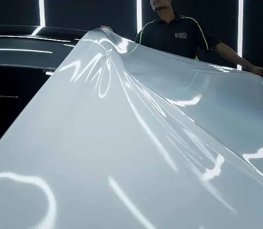 Technician applying a vinyl wrap film to a vehicle roof at System X Car Polish in Al Quoz, Dubai