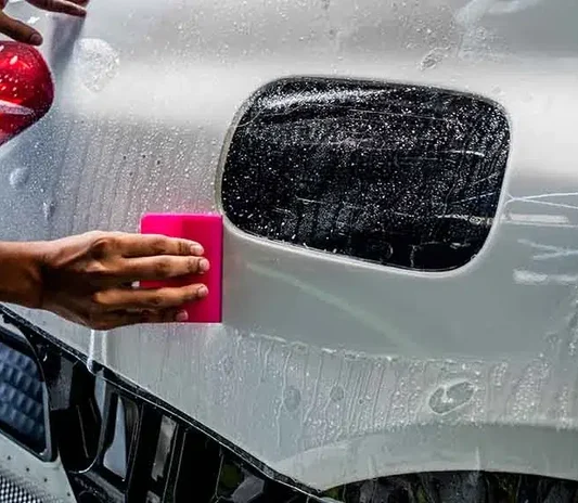 Technician using a pink squeegee to apply paint protection film near a fuel cap on a white car in Dubai